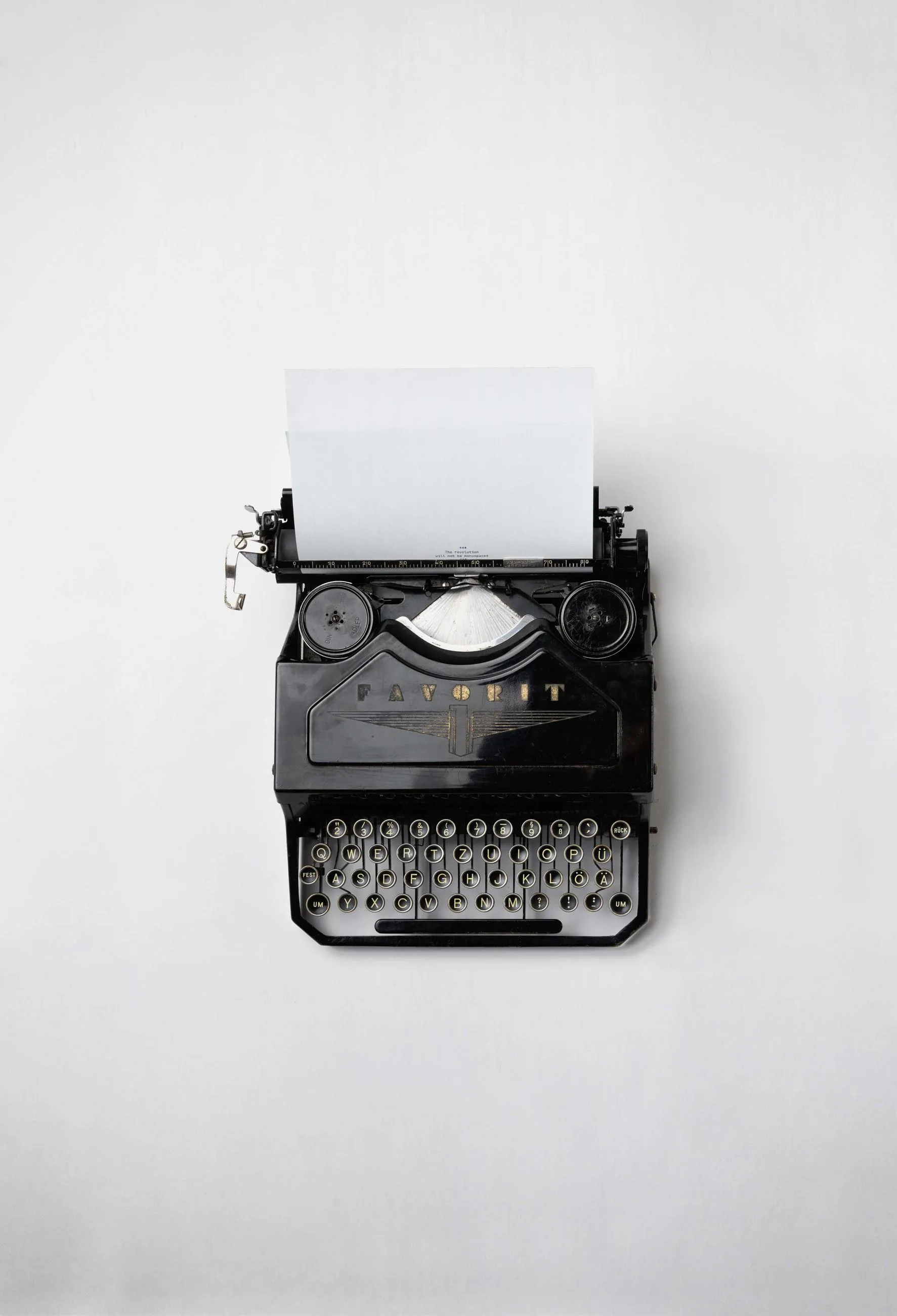 A black typewriter photographed from above on a white ground, a sheet of paper loaded.