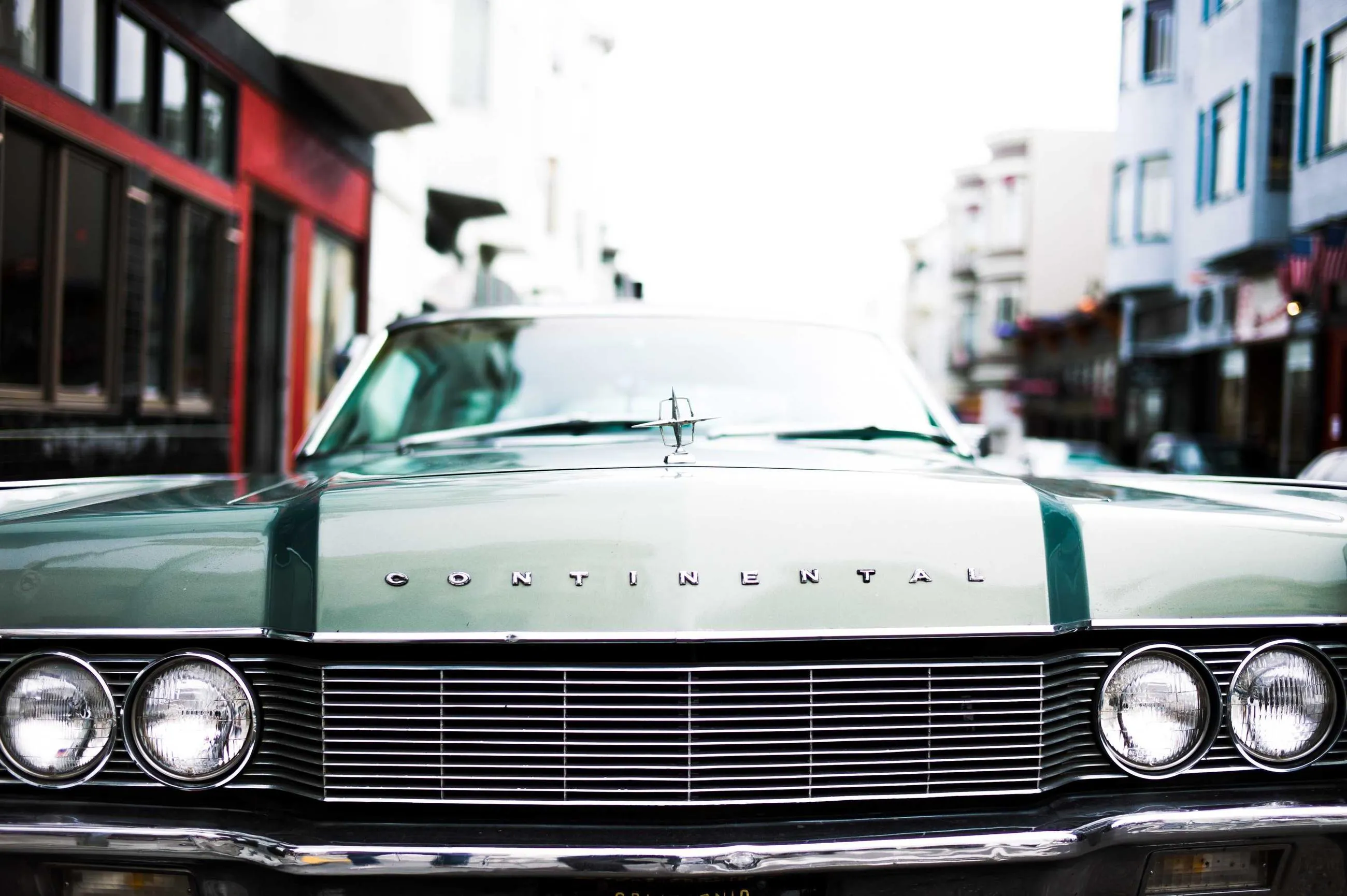 The chrome grille and quad headlamps of a green and white American saloon on a city street.