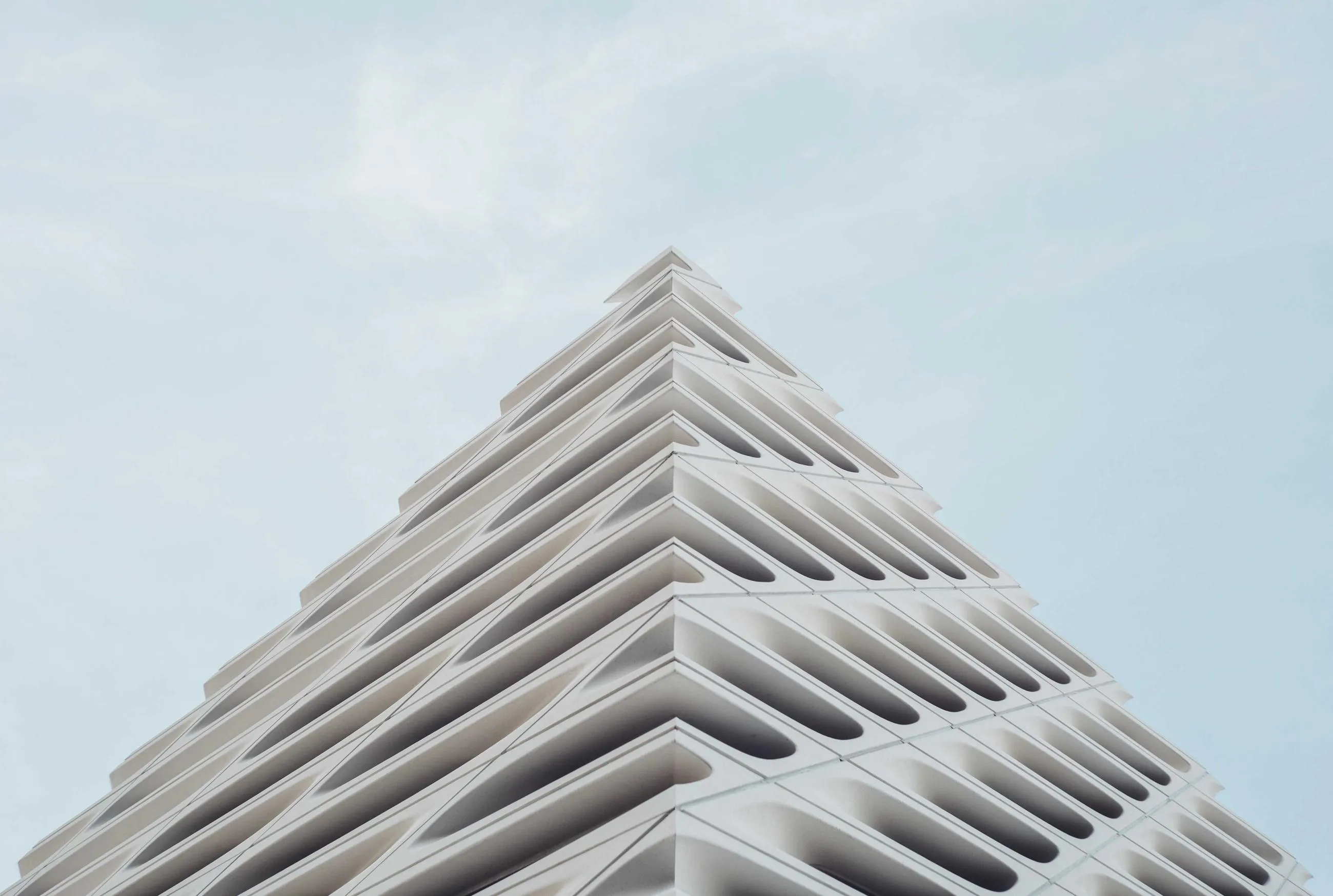 Stepped white balconies of a building rising into a pale blue sky.
