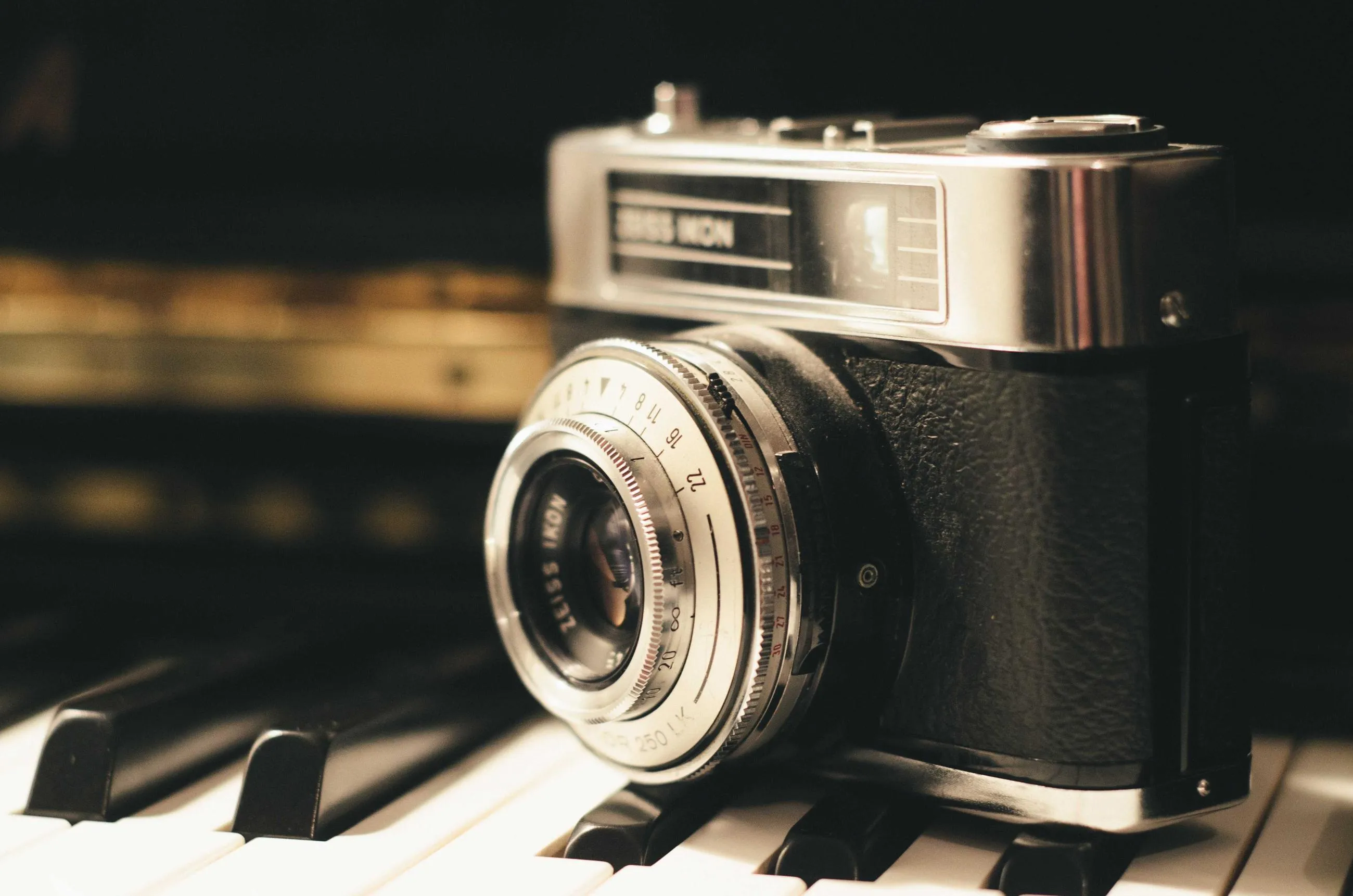 A silver rangefinder camera resting on piano keys.