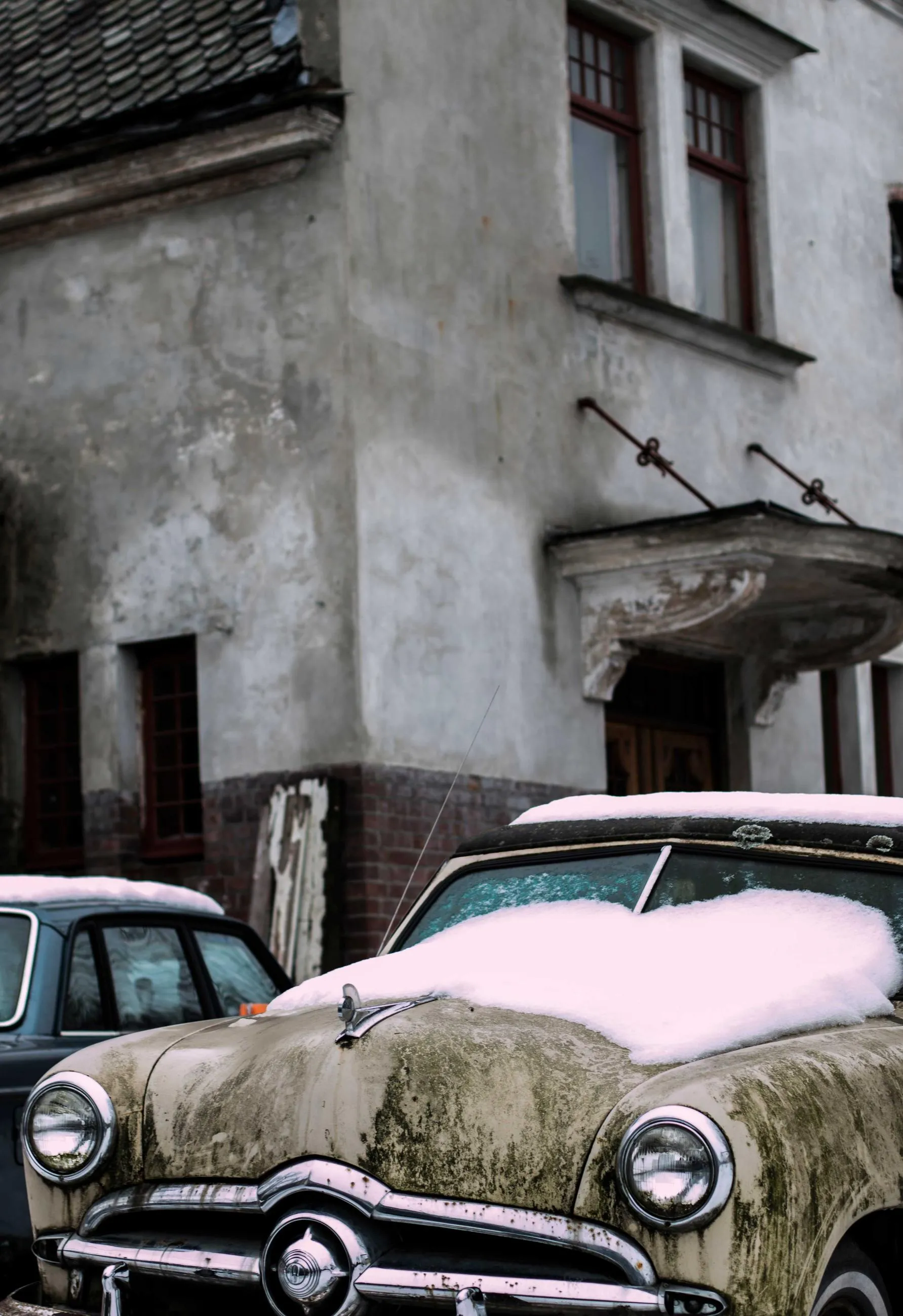 A pink-roofed 1950s car parked tight against a grey townhouse.
