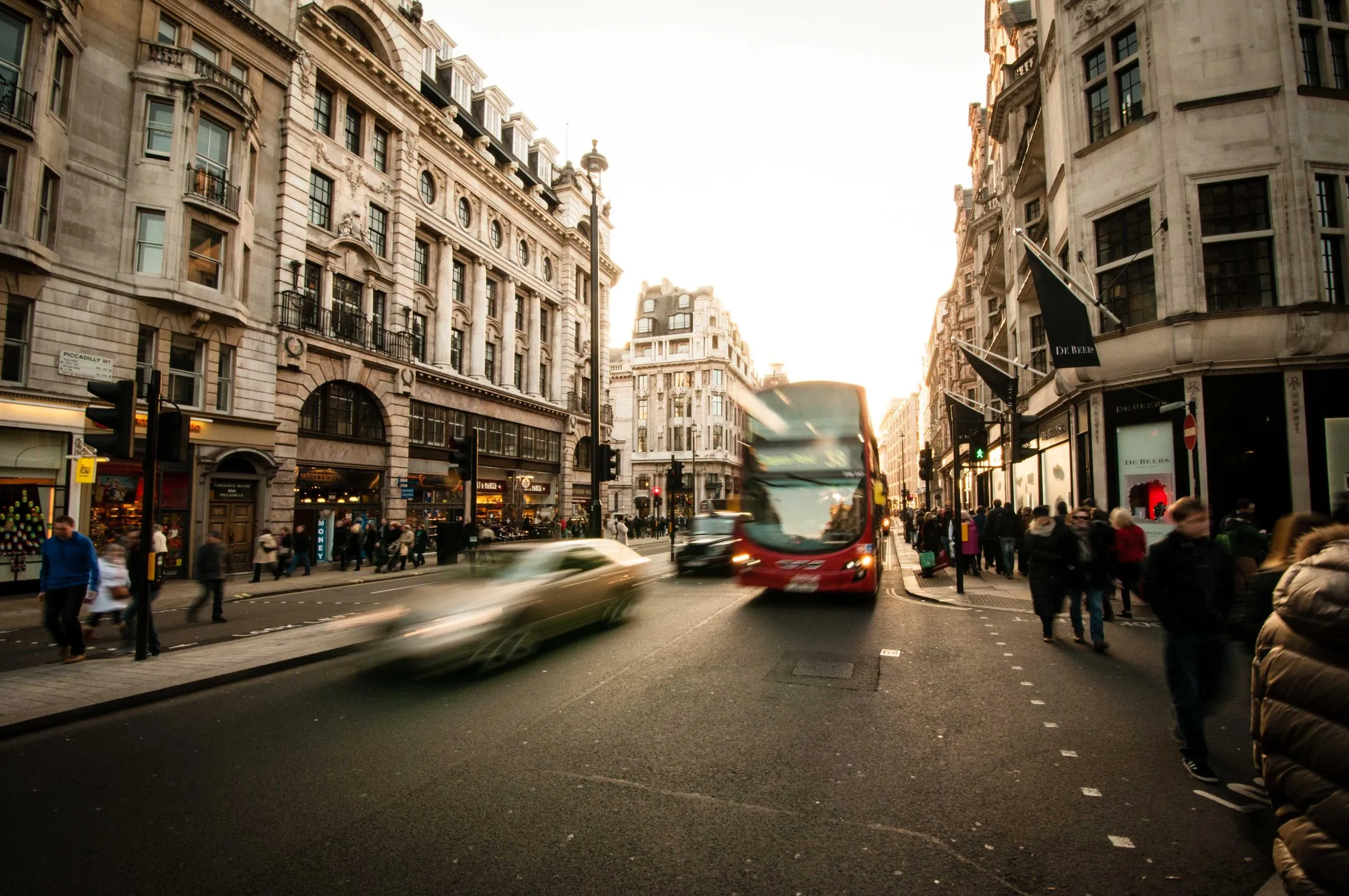 A red double-decker bus and a blurred taxi on a London street lined with stone buildings.