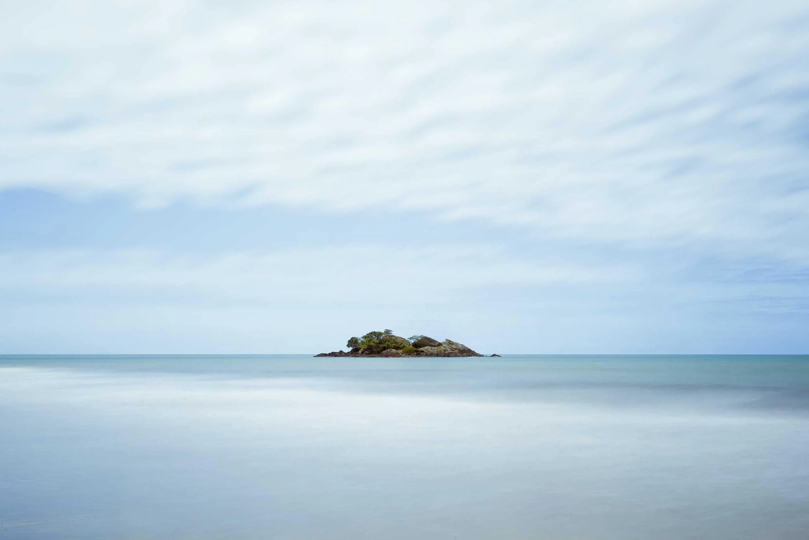 A small rocky island on a calm turquoise sea, smoothed by a long exposure.