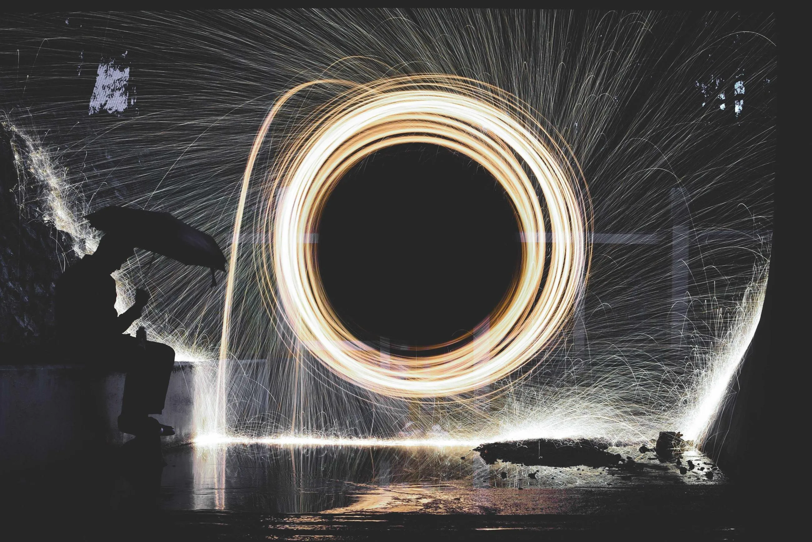 A ring of sparks from spun steel wool frames a figure holding an umbrella.