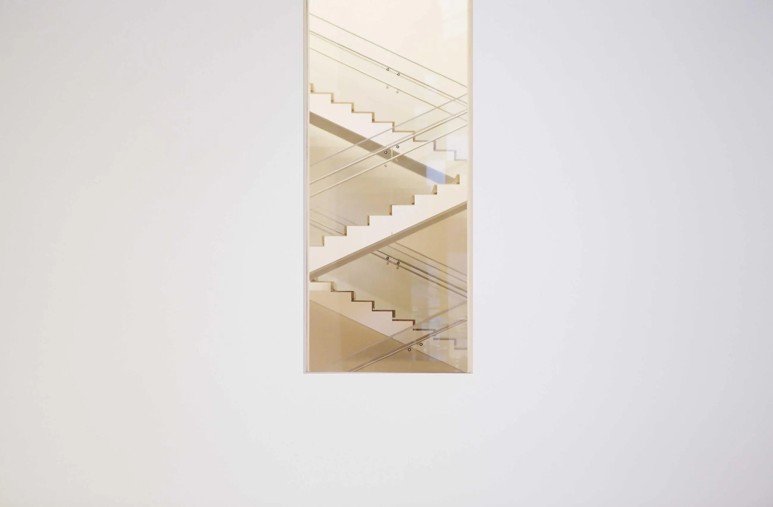 A narrow window in a white wall reveals a staircase climbing out of view.