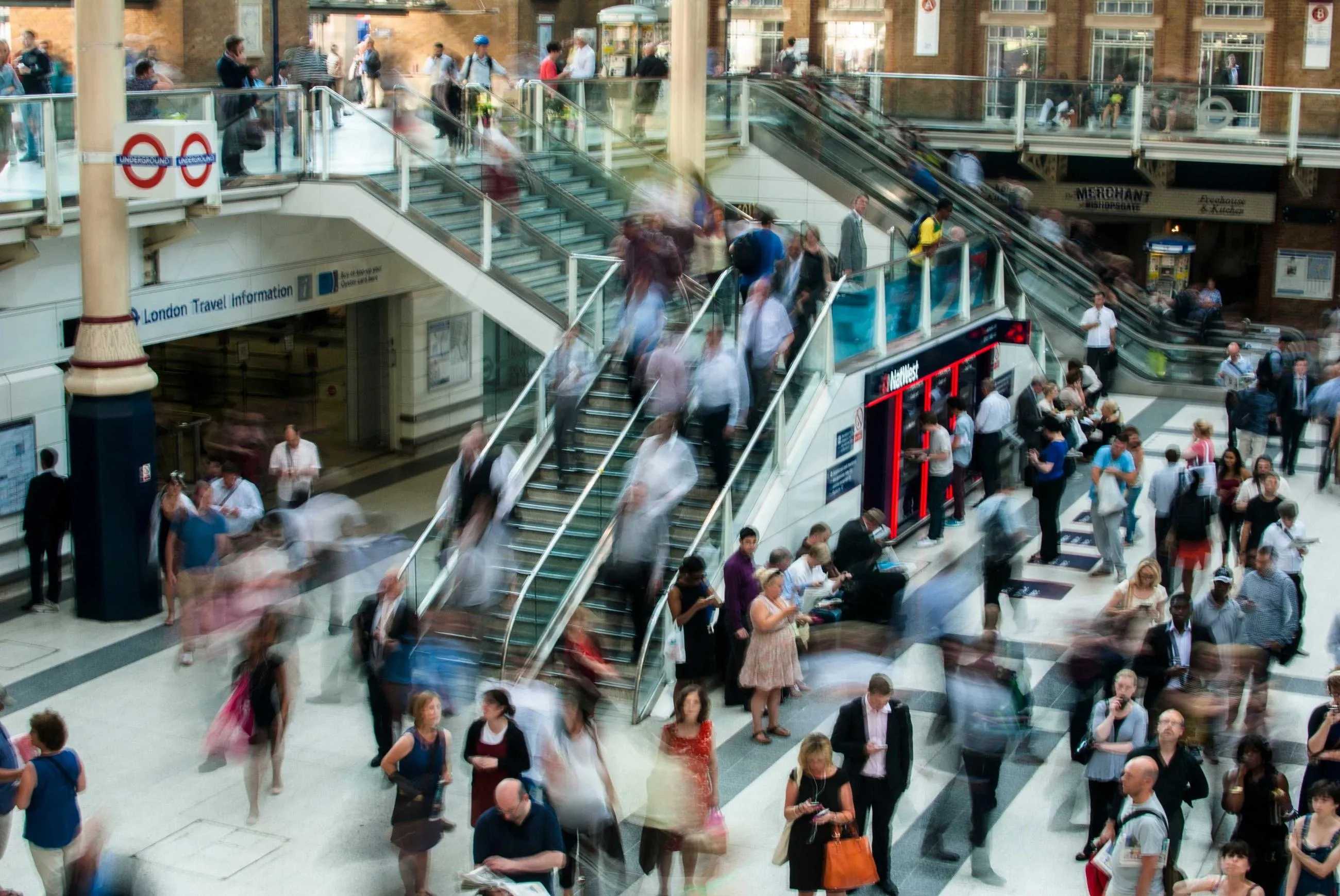 Crowds rush across escalators and walkways inside an Underground station.
