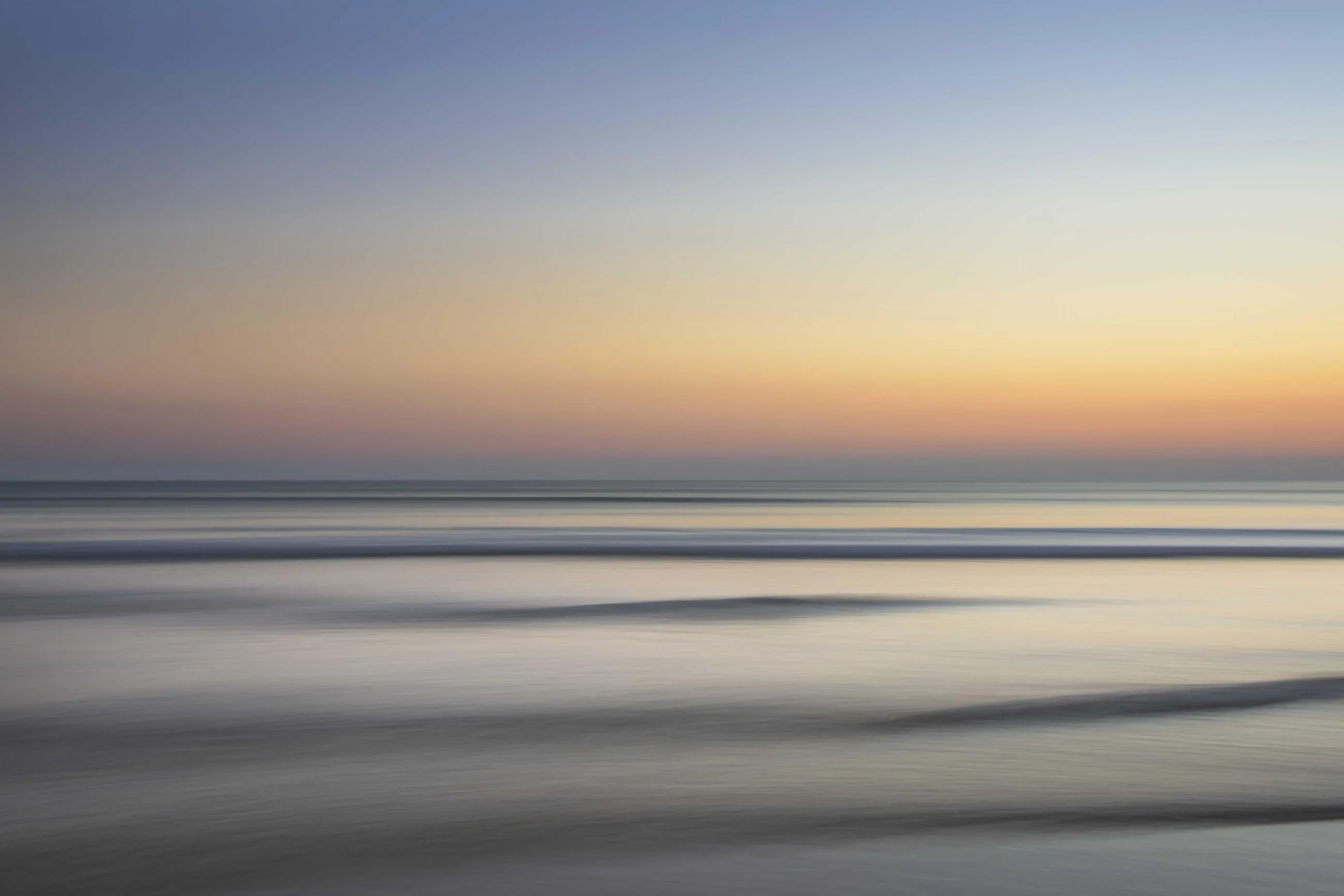 Waves smoothed to mist on a shoreline under a pale dawn sky.