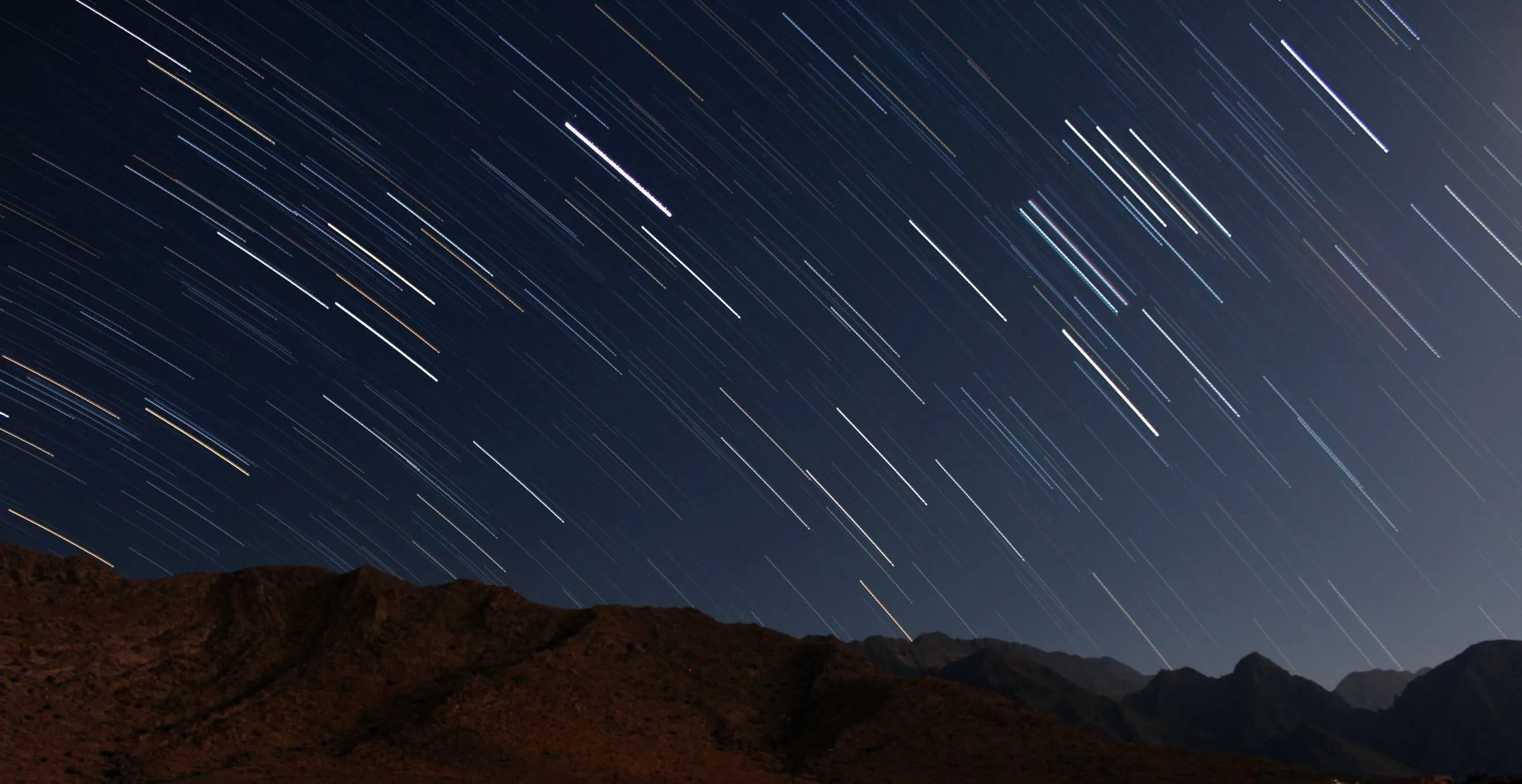 Diagonal star trails over a dark mountain ridge.