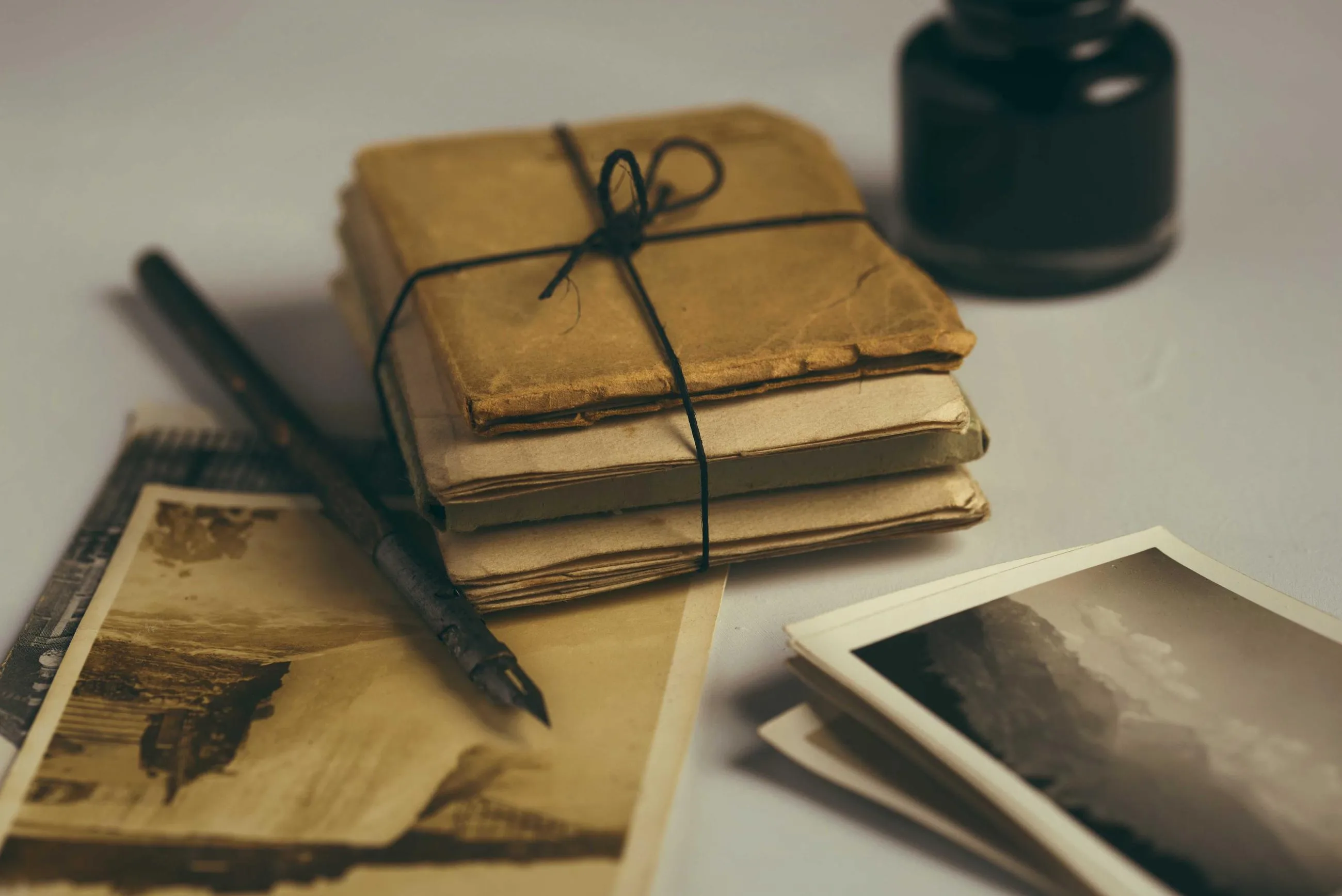 A bundle of old letters tied with string beside a pen and two photographs.