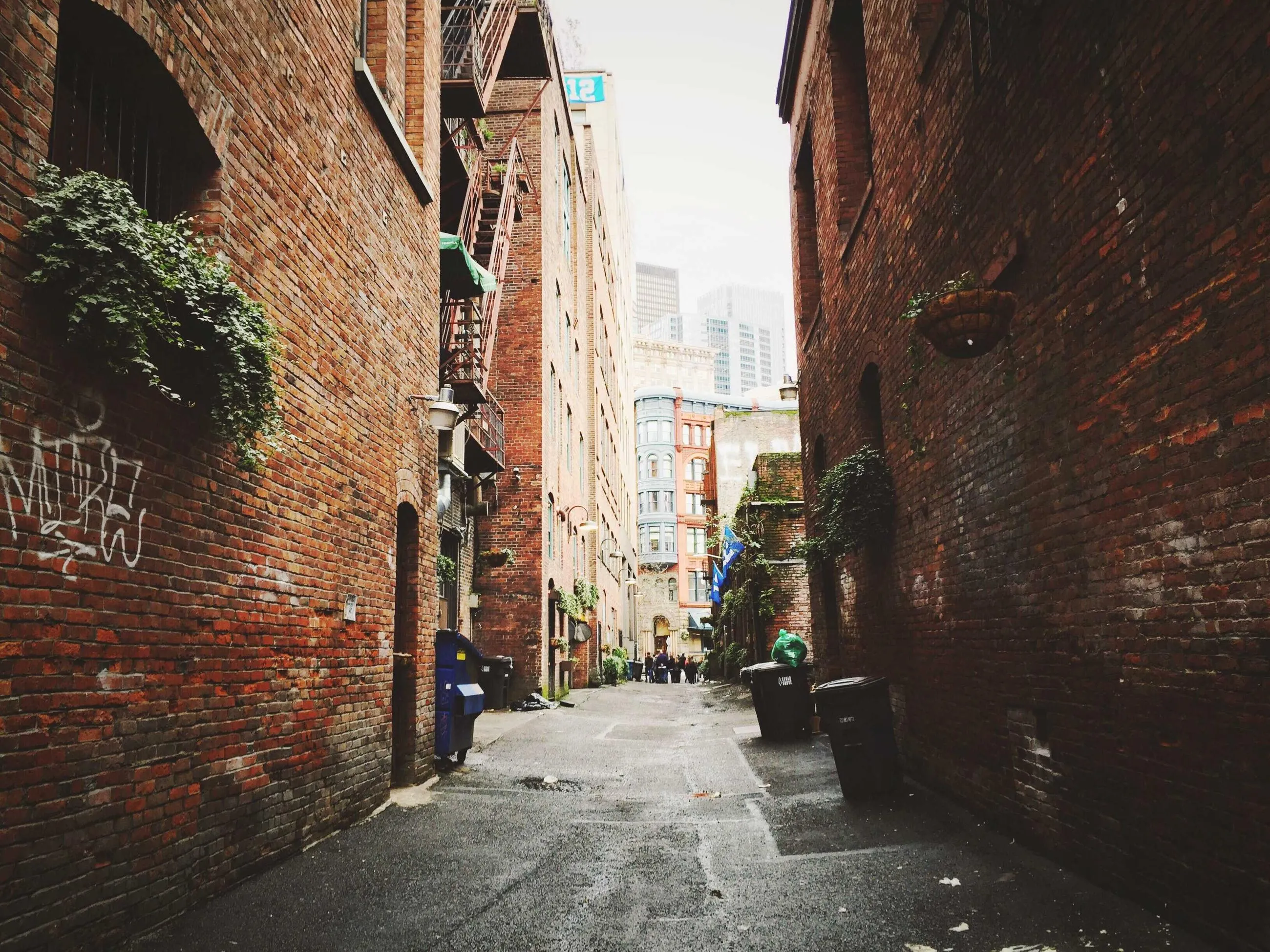 A narrow brick alley between tall buildings, empty except for a figure at the far end.